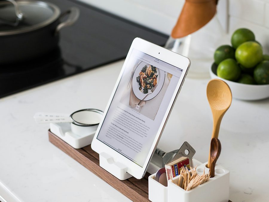 A tablet propped on a kitchen counter showing a recipe, beside a wooden spoon and a bowl of limes